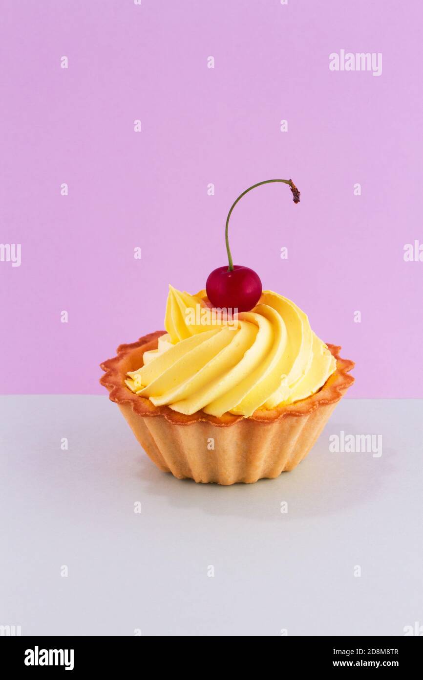 A bright ripe cherry berry on the top of a delicious cake on a double pastel purple-turquoise background. Stock Photo