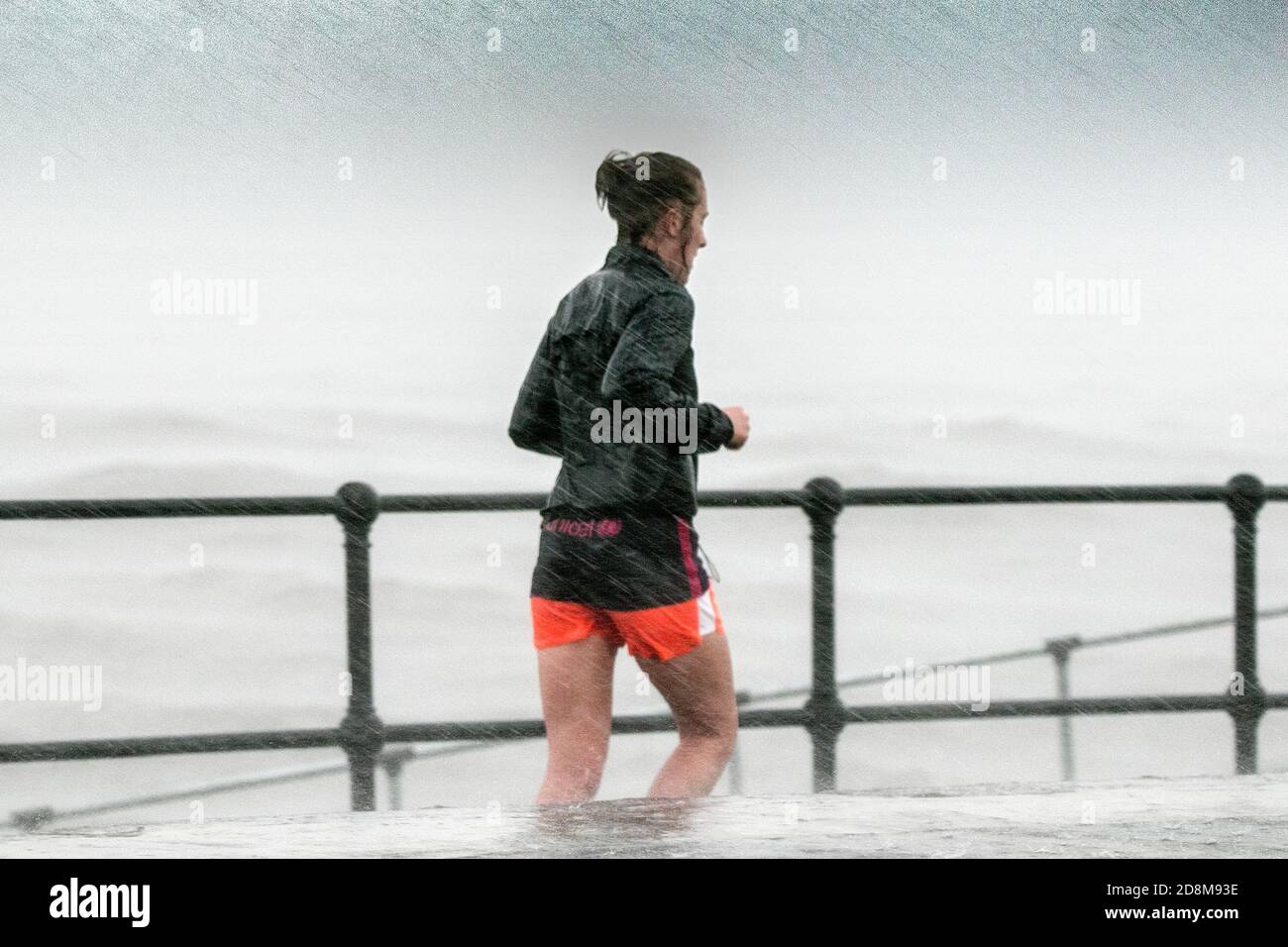 Crosby, Merseyside, 31 October 2020.  A brave woman jogs along the promenade as storm force winds and high tide collide to batter the north west coastline at Crosby in Merseyside.   Credit: Cernan Elias/Alamy Live News Stock Photo