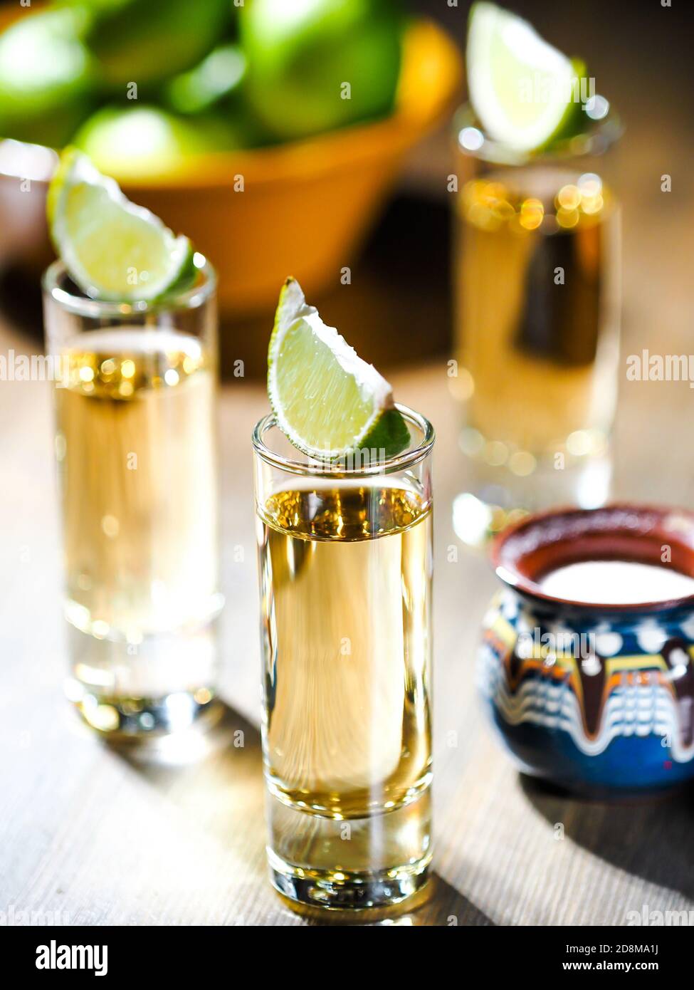 Three shots of tequila in tall shot glasses with lime wedges on top