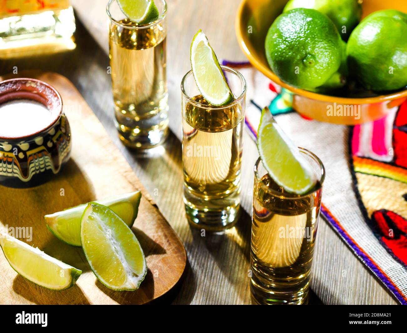 Three shots of tequila in tall shot glasses with lime wedges on top