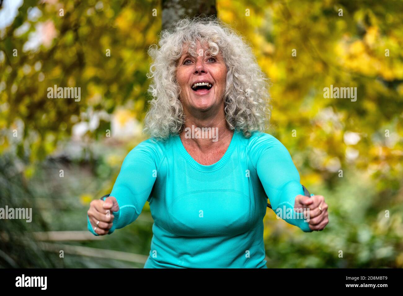 A woman in her sixties exercises outdoors with a resistance band in autumn. Stock Photo