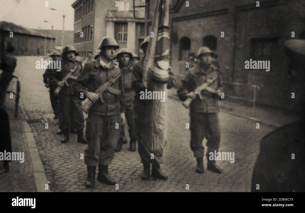 East Berlin, German Democratic Republic, 1970. Soviet officer looks at a group of East German soldiers with weapons and a flag before a parade Stock Photo