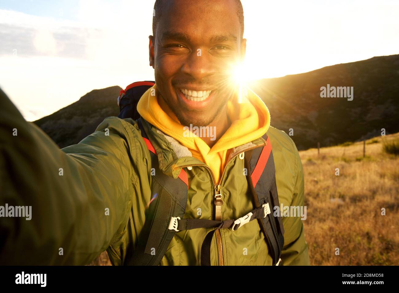 Portrait of happy black man hiking and taking selfie with sunset in ...