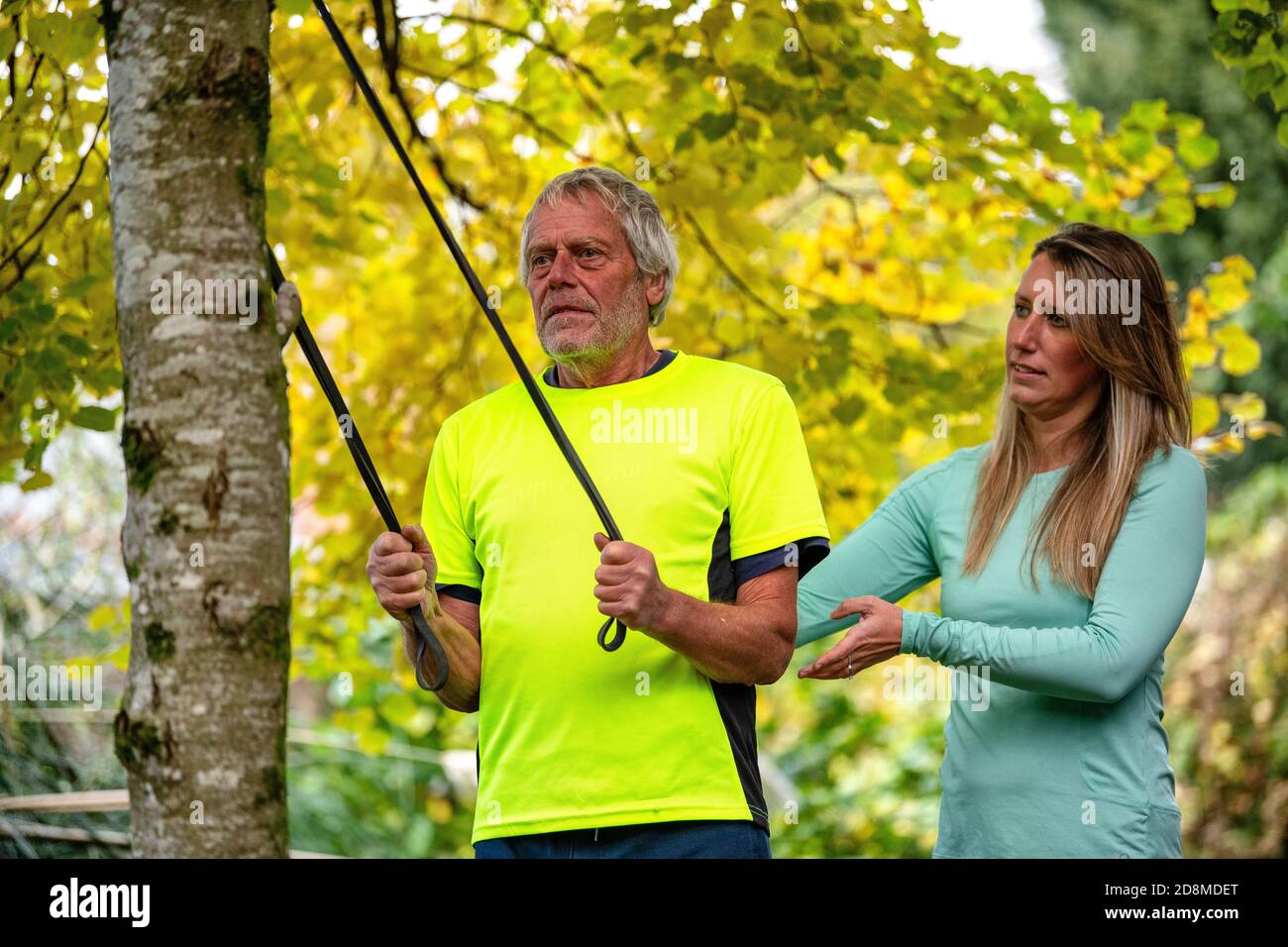 A man in his late sixties exercises outdoors with a resistance band