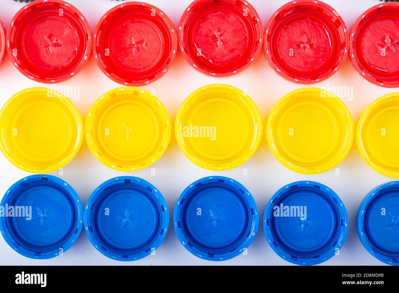 Plastic multi-colored bottle caps are arranged in rows on a white