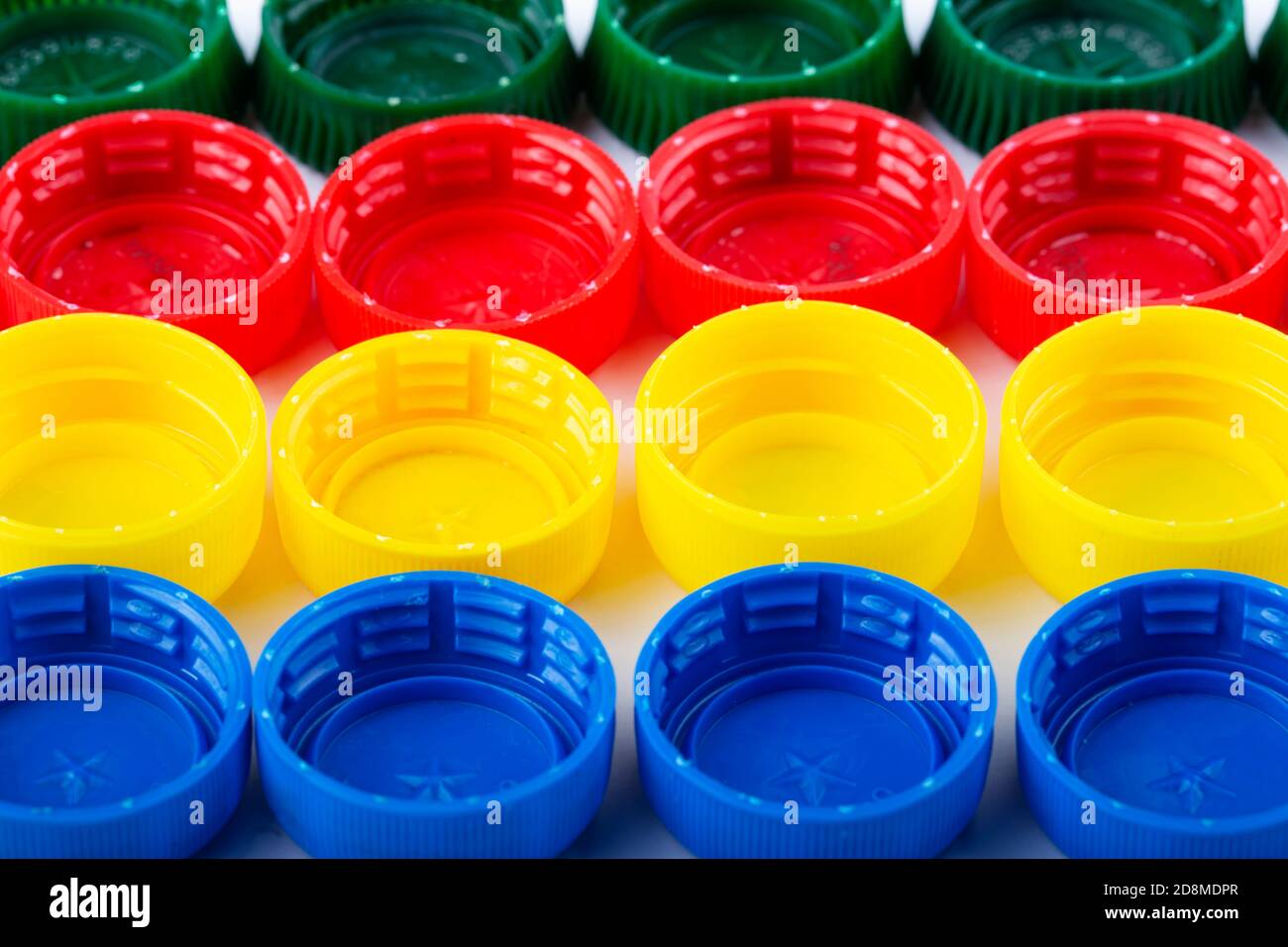 Plastic multi-colored bottle caps are arranged in rows on a white