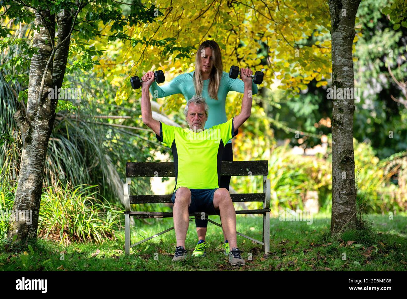 A man in his late sixties lifts weights outdoors with the help of a
