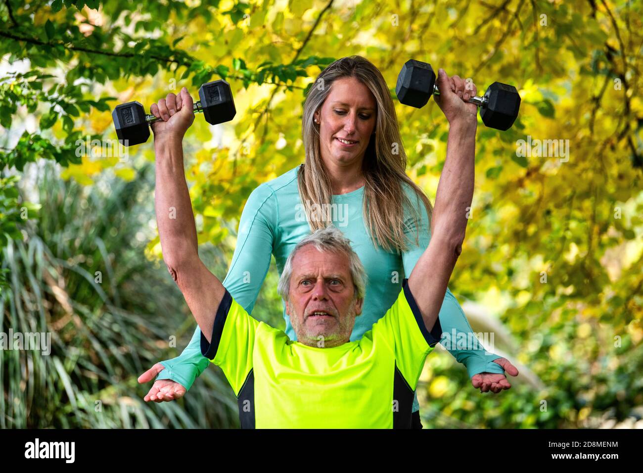 A man in his late sixties lifts weights outdoors with the help of a