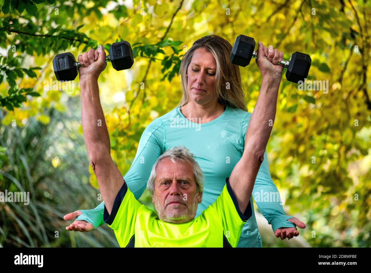 A man in his late sixties lifts weights outdoors with the help of a