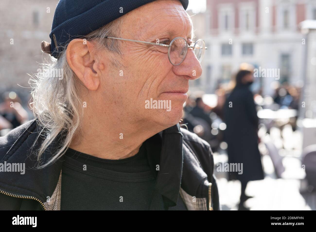 Portrait of an elderly long white haired artist wearing glasses and black hat in the square. Stock Photo