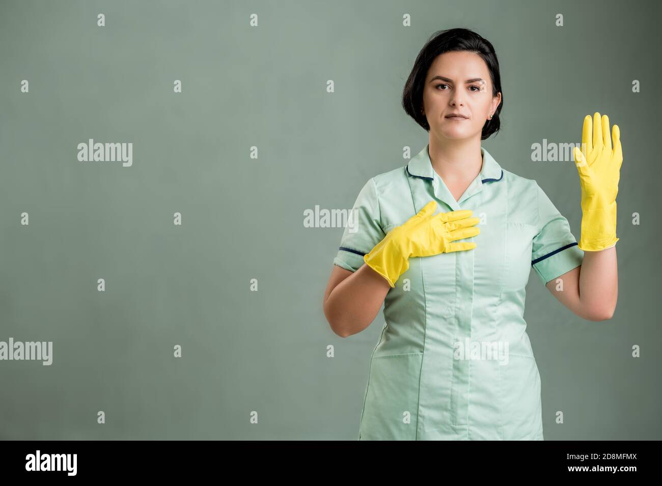 Young cleaning woman wearing a green shirt and yellow gloves, showing ...