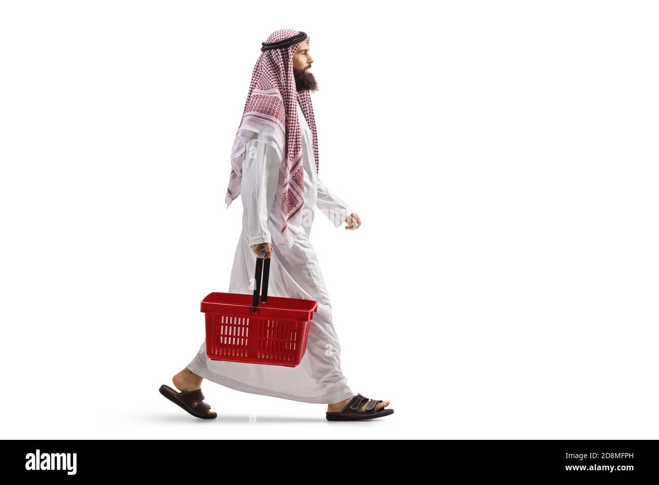 Full length profile shot of an arab man in a thobe walking with a shopping basket isolated on white background Stock Photo