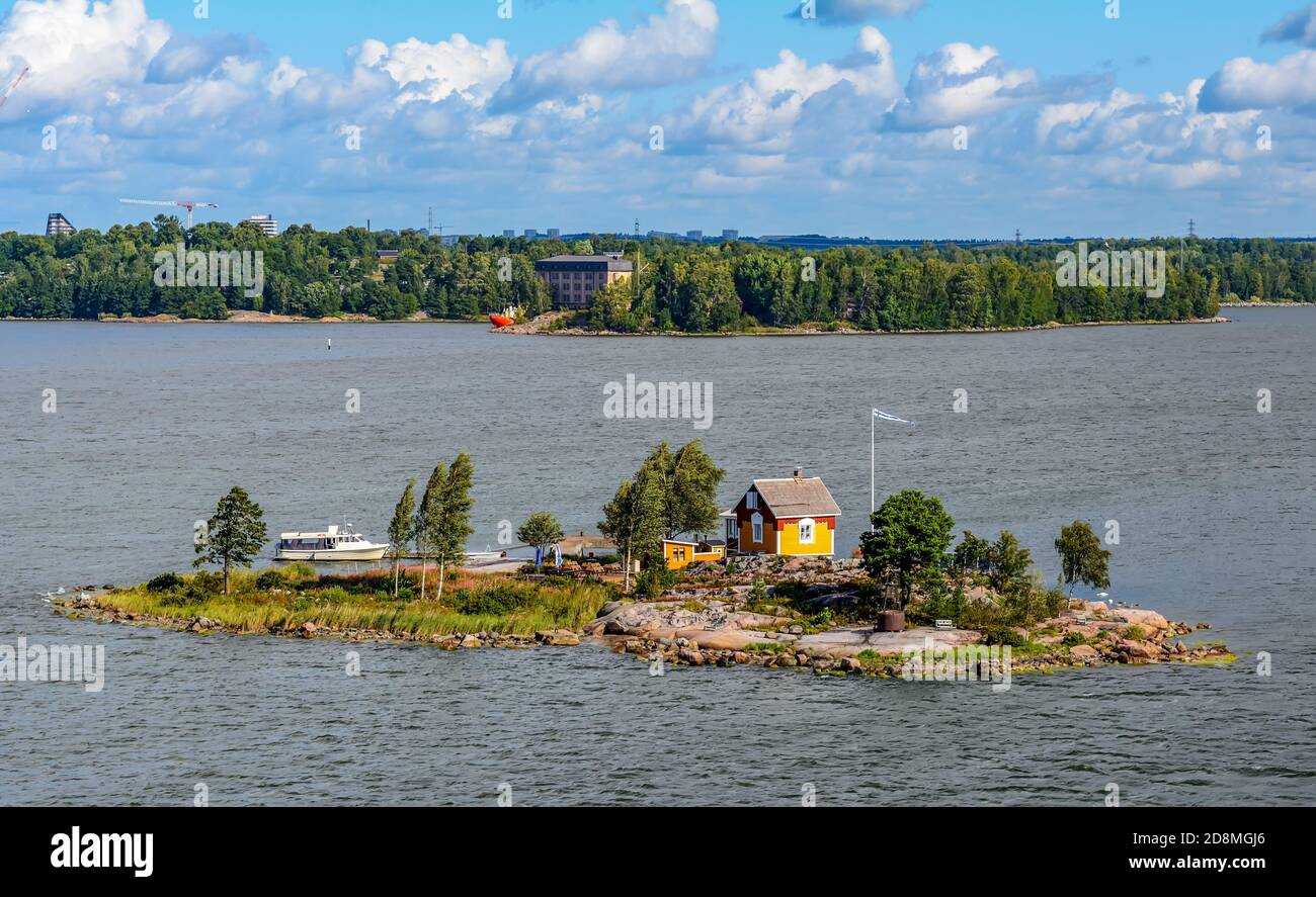 Small rocky island with little yellow wooden house and flag of Finland Stock Photo