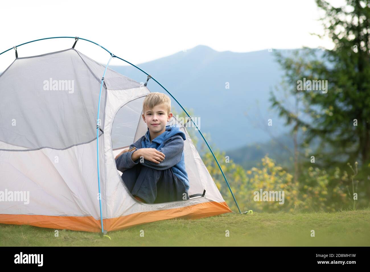 Happy child boy resting alone in a tent at mountain campsite enjoying ...