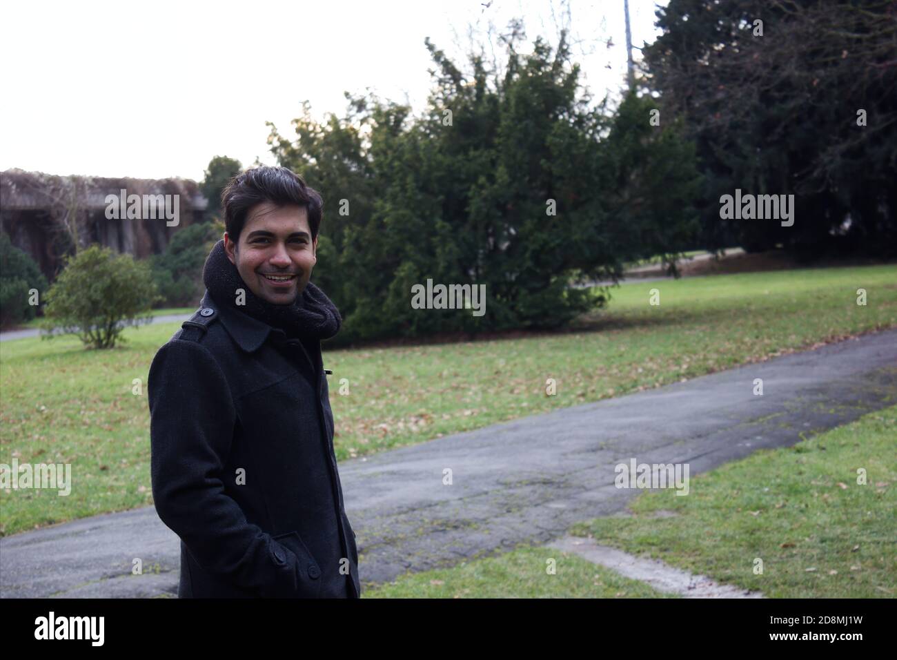 An asian ethnicity Indian man smiling in a coat and scarf during winters in a park / outdoor Stock Photo