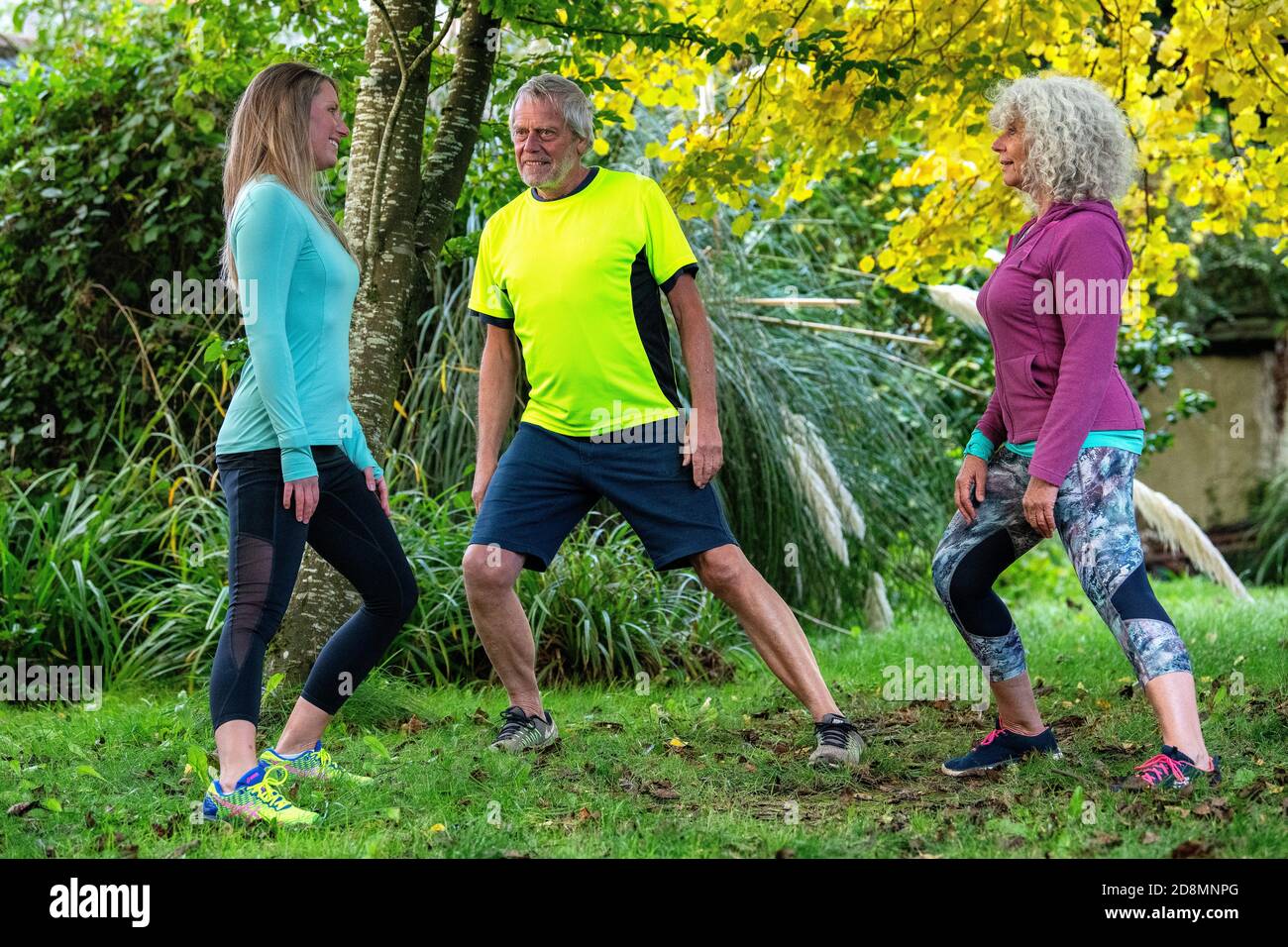 A couple in their sixties exercise with a young female personal trainer outdoors. Stock Photo