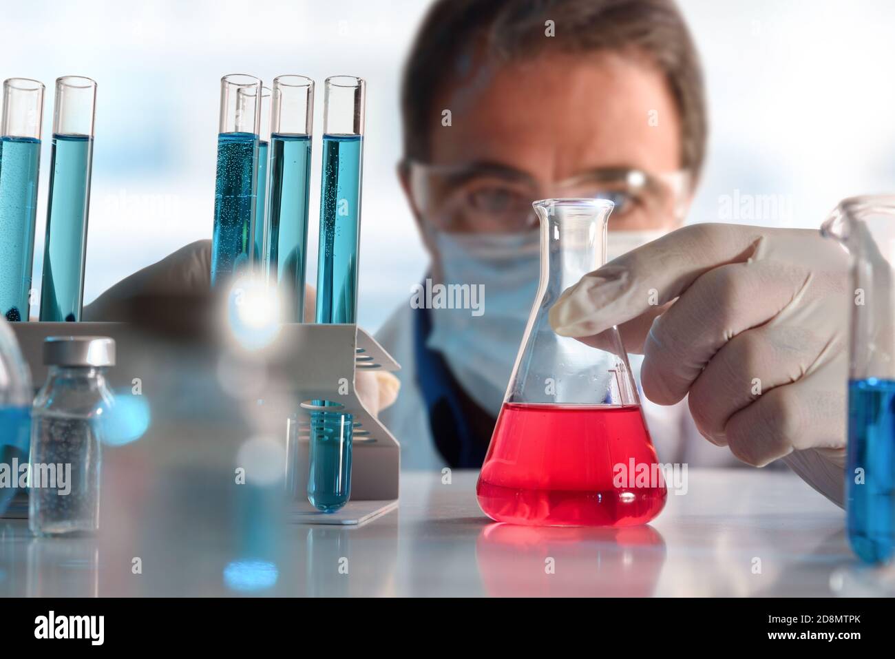 Detail of scientist looking carefully at a red liquid in a flask on a ...