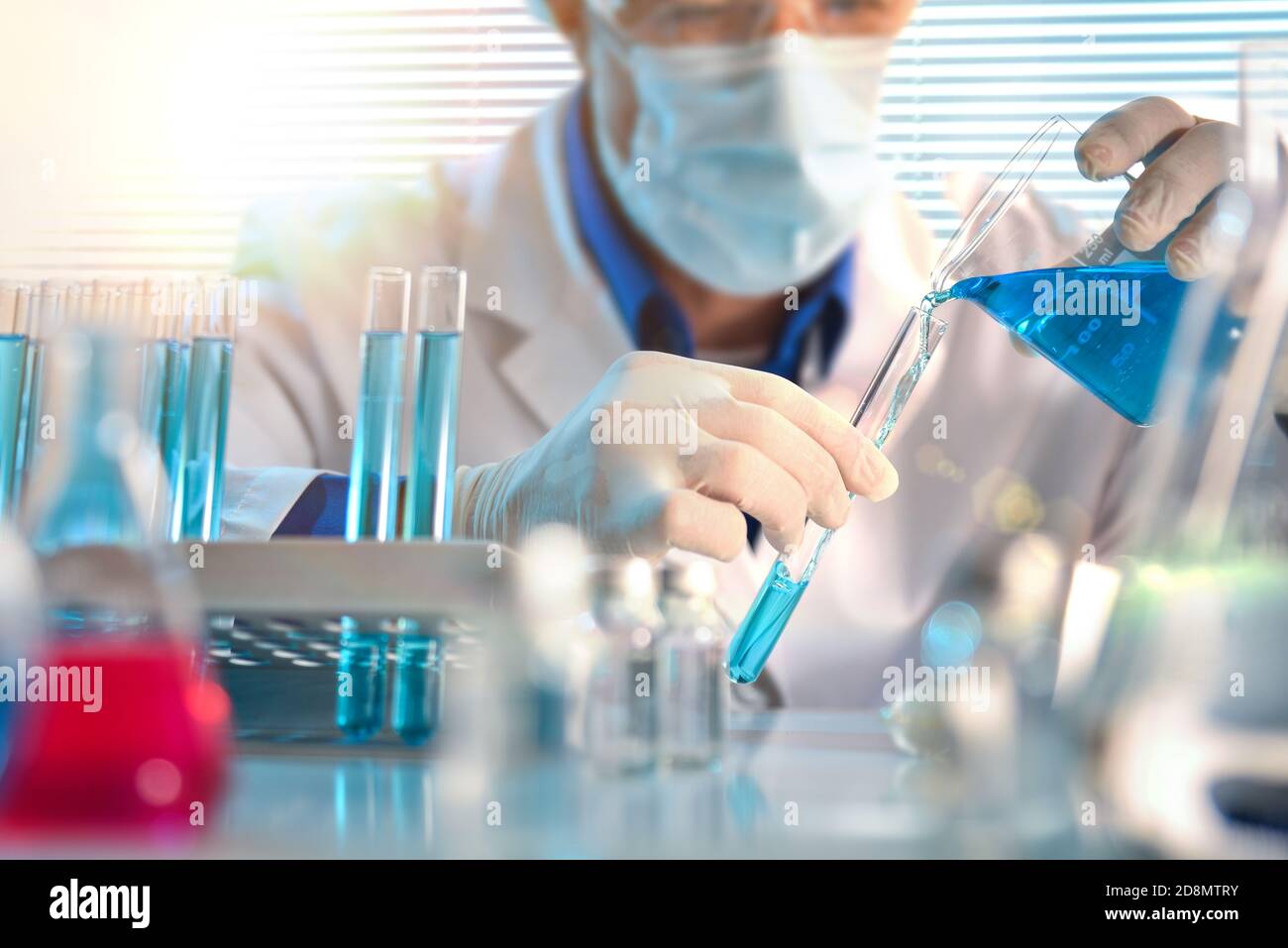 Scientist pouring blue liquid from a beaker into a test tube close up ...