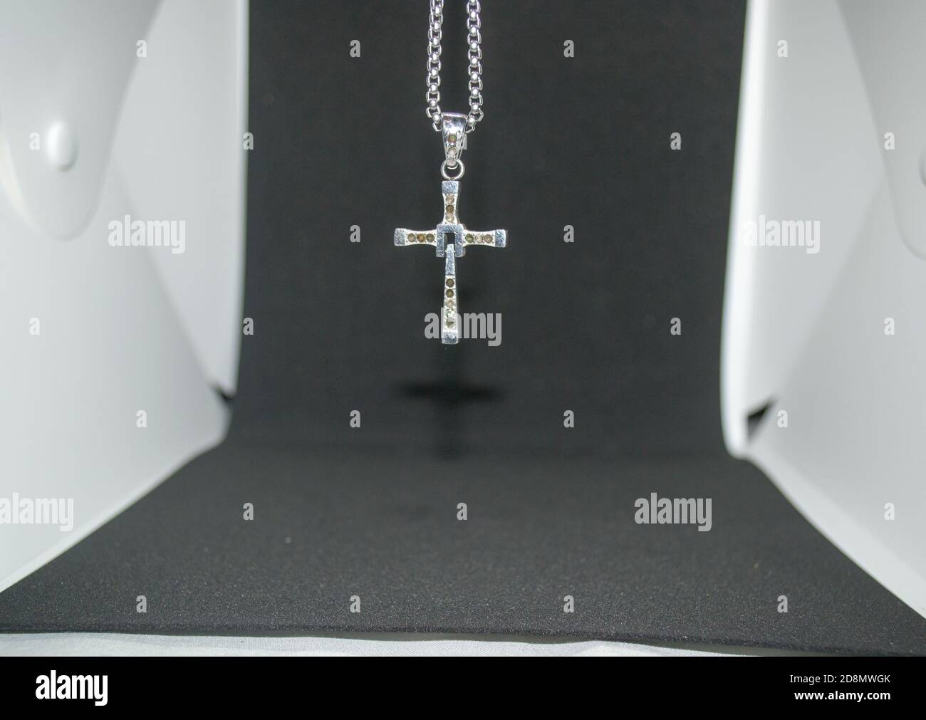 Close-up image of a silver metal christian cross necklace/pendant or silver metal crucifix necklace/pendant hanging on a black and white background Stock Photo