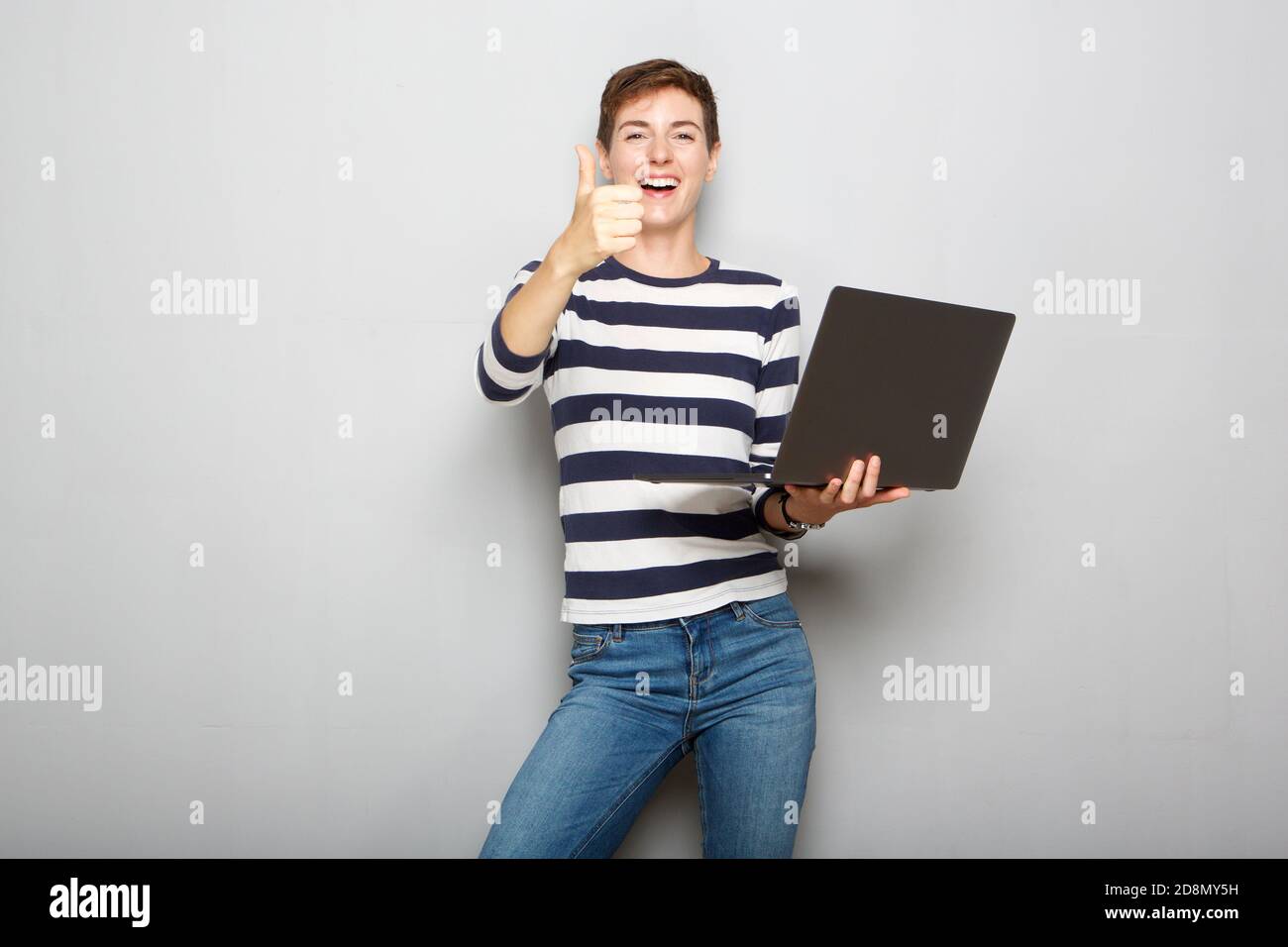 Portrait of cool young woman holding laptop and with thumbs up hand ...
