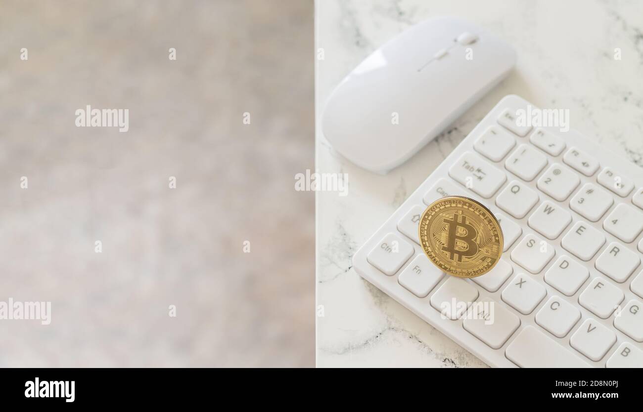 Cryptocurrency gold bitcoin on white computer keyboard next to mouse on marble table Stock Photo