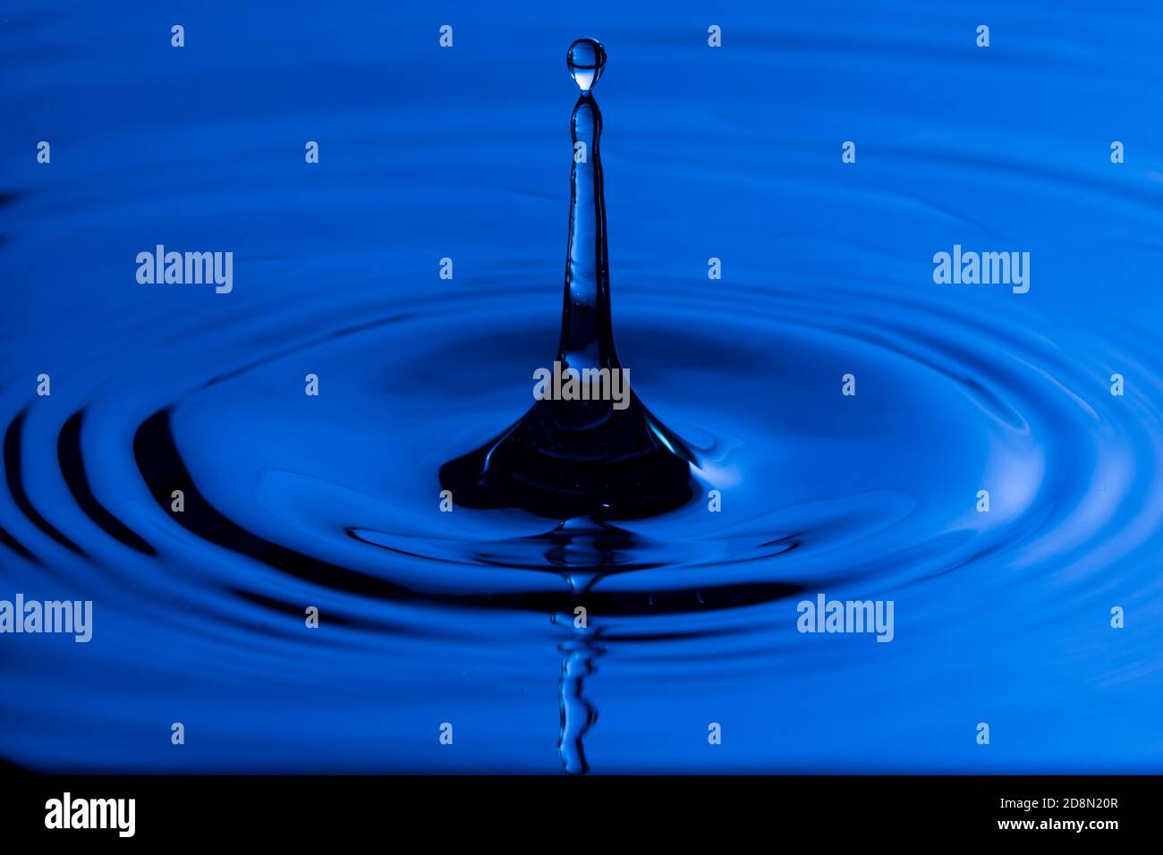 Perfect water drop splashing into smooth water causing ripples Stock