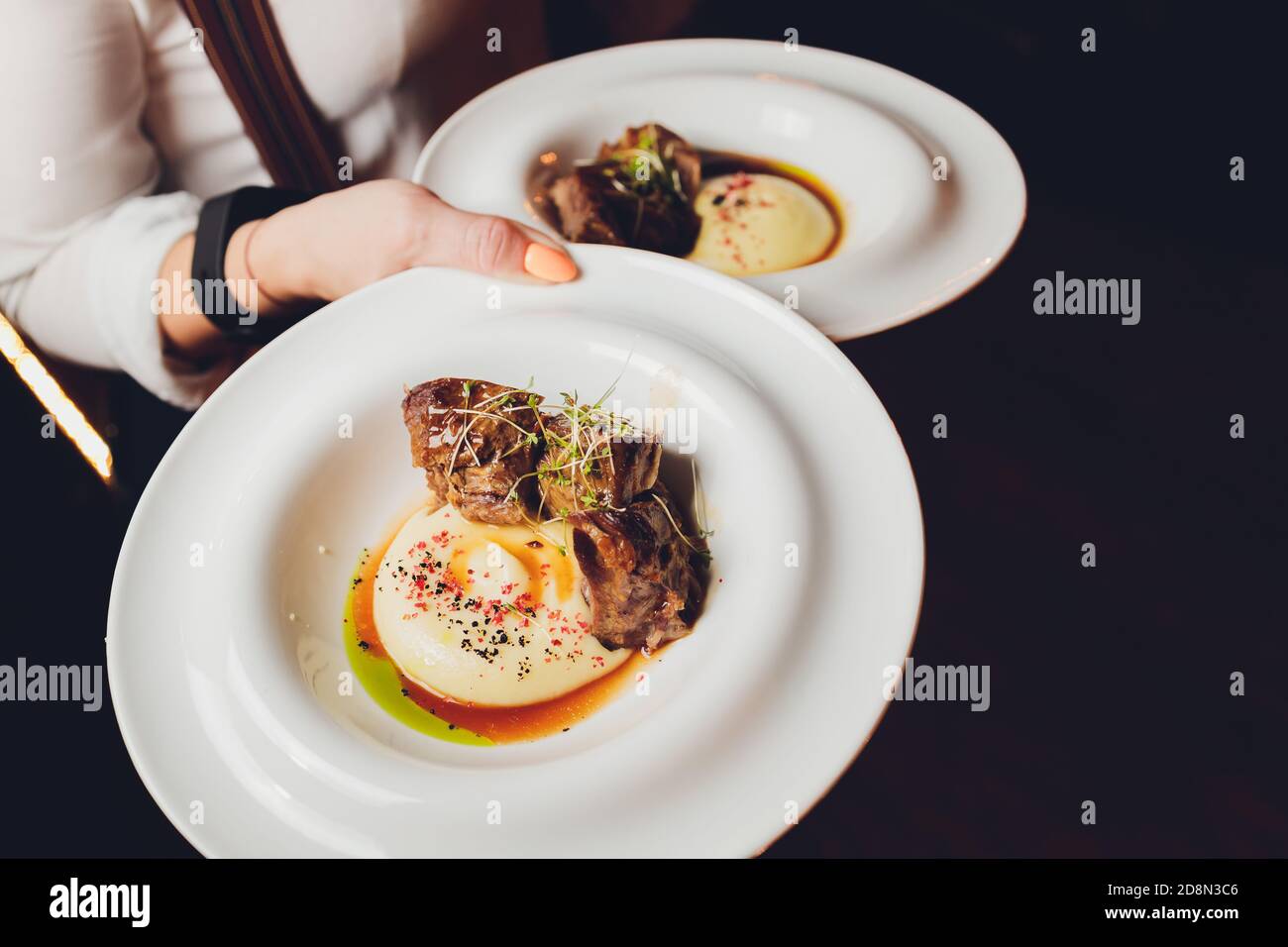 The waiter is holding a plate Delicious juicy meat cutlets, mashed potatoes sprinkled with greens and fresh healthy salad of tomatoes and lettuce Stock Photo