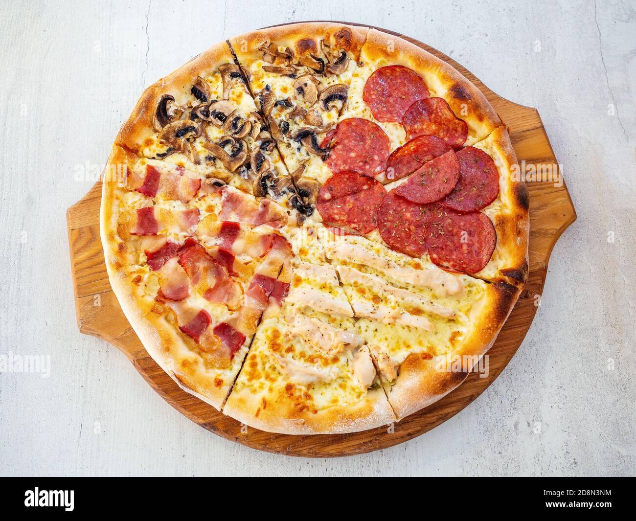 Round pizza with four different fillings cut into pieces on a wooden tray. Top view Stock Photo