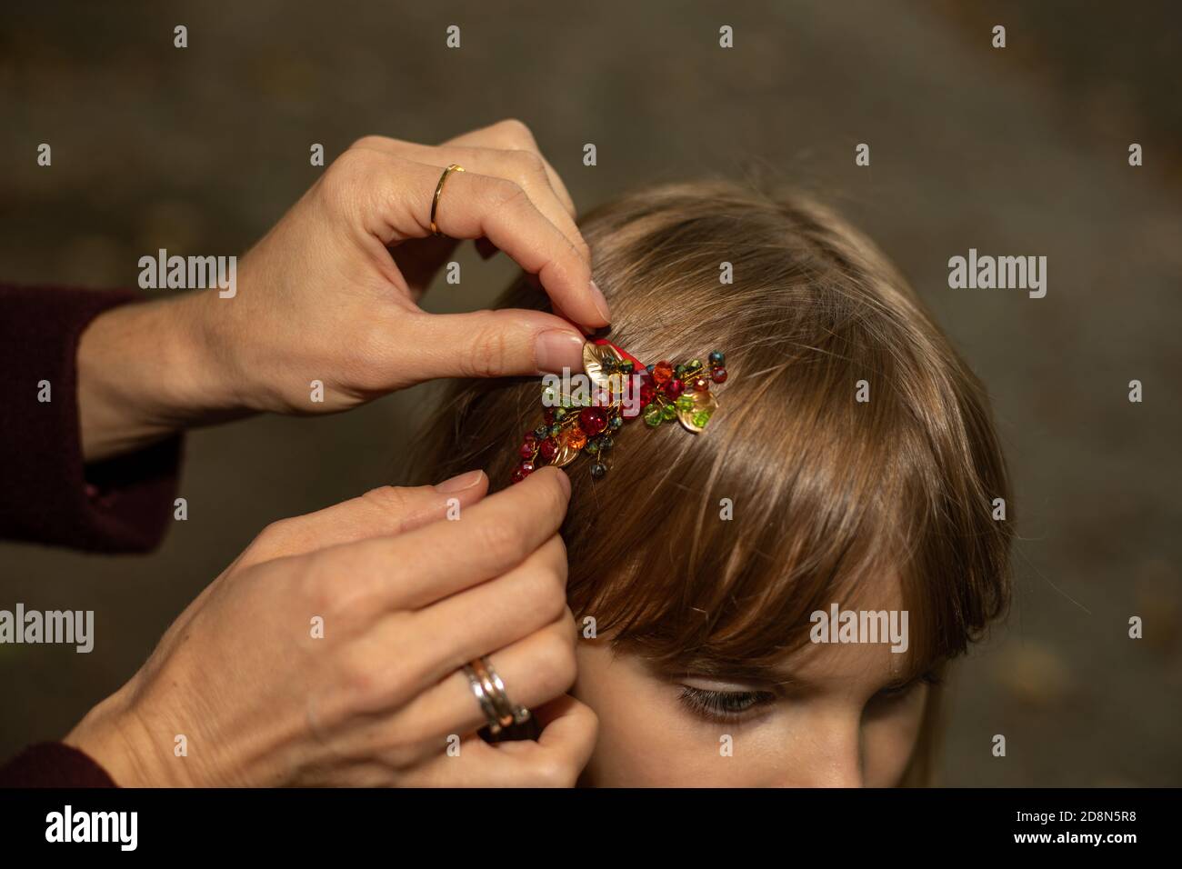 Women's hands of a mother or caregiver carefully fasten a hair clip on the hair of a little girl outdoors. Hair accessories Stock Photo