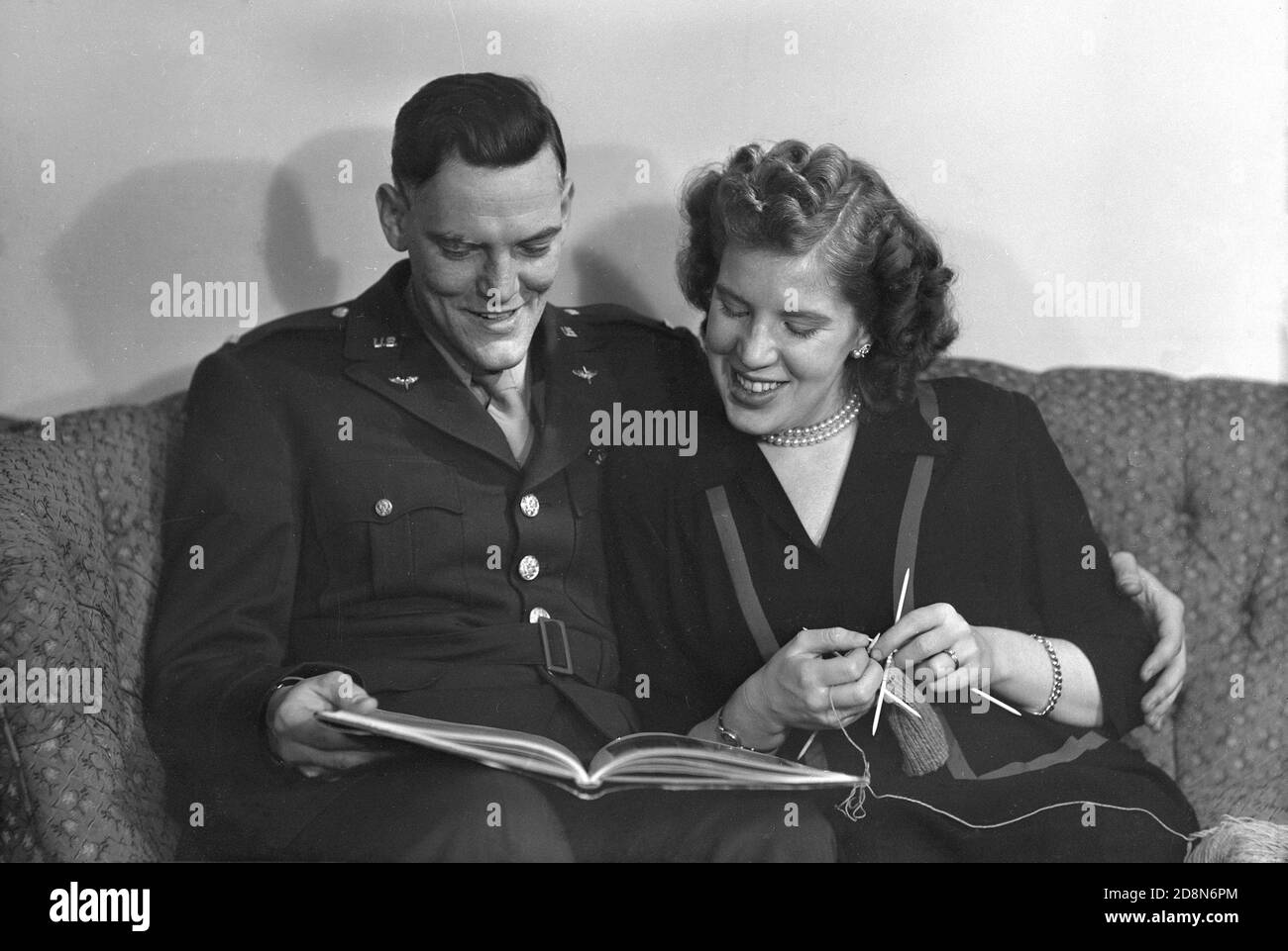 1940s, historical, a uniformed US Army officer sitting ona sofa looking at a book, with his wife beside him holding needles and wool in her hand, knitting, USA. Stock Photo