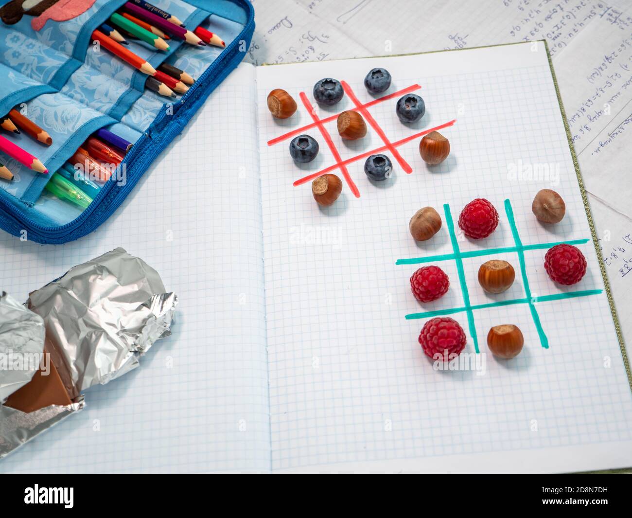 Tasty school break and fun games at school. Tic-tac-toe by raspberries, blueberries and hazelnuts. Pencil case with colored pencils and chocolate. Stock Photo