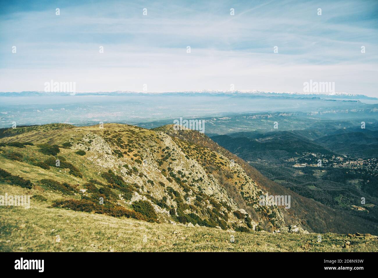 Landscape of a yellowish peak with an extension of green fields below and a snowy mountain range far on the background Stock Photo
