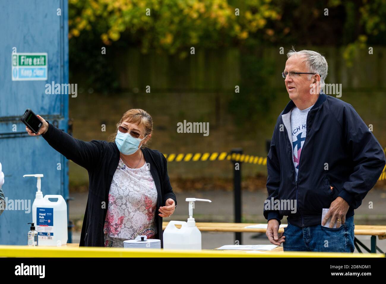 A woman wearing a facemask gives directions to a man as he enters Champion Hill to watch Dulwich Hamlet FC Women. Stock Photo