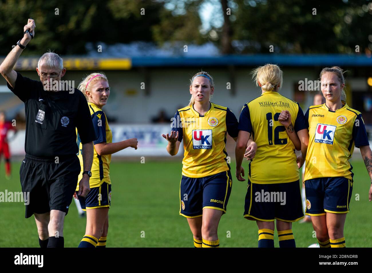 A referee guides four female footballers forming a wall ten meters from a free kick. Stock Photo