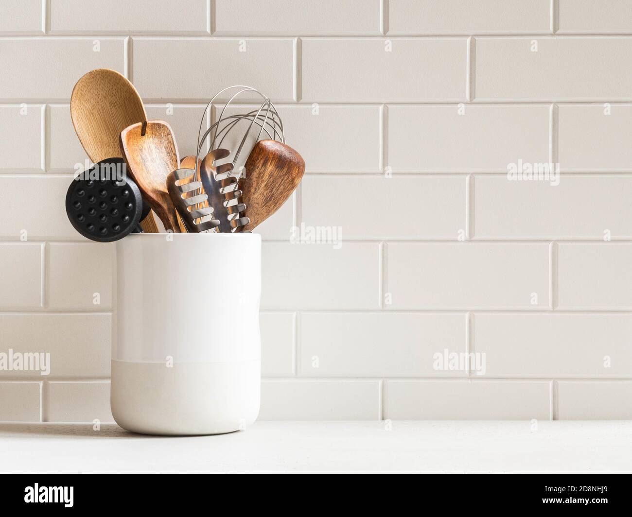 Stylish white kitchen background with kitchen utensils in ceramic jar on white countertop, copy space for text, front view Stock Photo