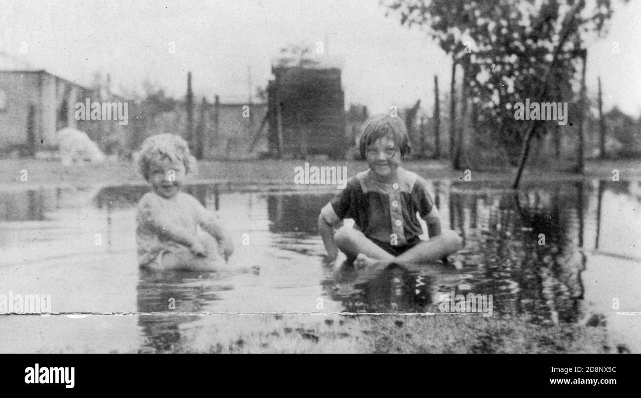 Two children, George and Cecelia McKechnie, playing in a large puddle in their yard in Charleville, Queensland, Australia, 1931. From the McKechnie family collection. Stock Photo