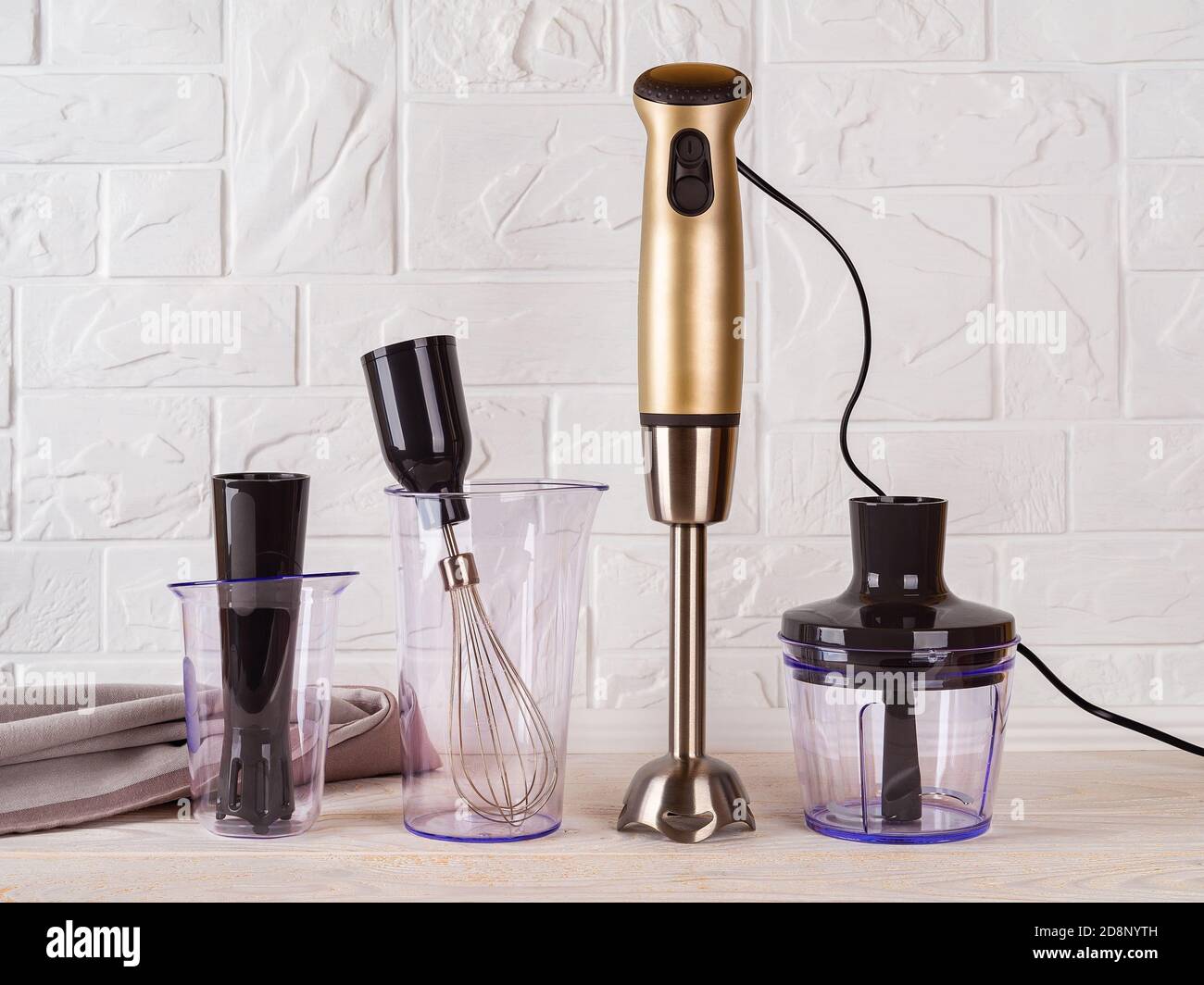 Immersion hand blender with different attachments and two cups on wood table. Electric kitchen appliances for making sauces, smoothies, puree. Stock Photo