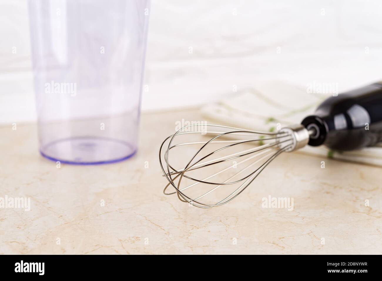 Close-up of immersion hand blender whisk for whipping and cup on a table. Modern electric kitchen appliances for making sauces, smoothies, puree. Stock Photo