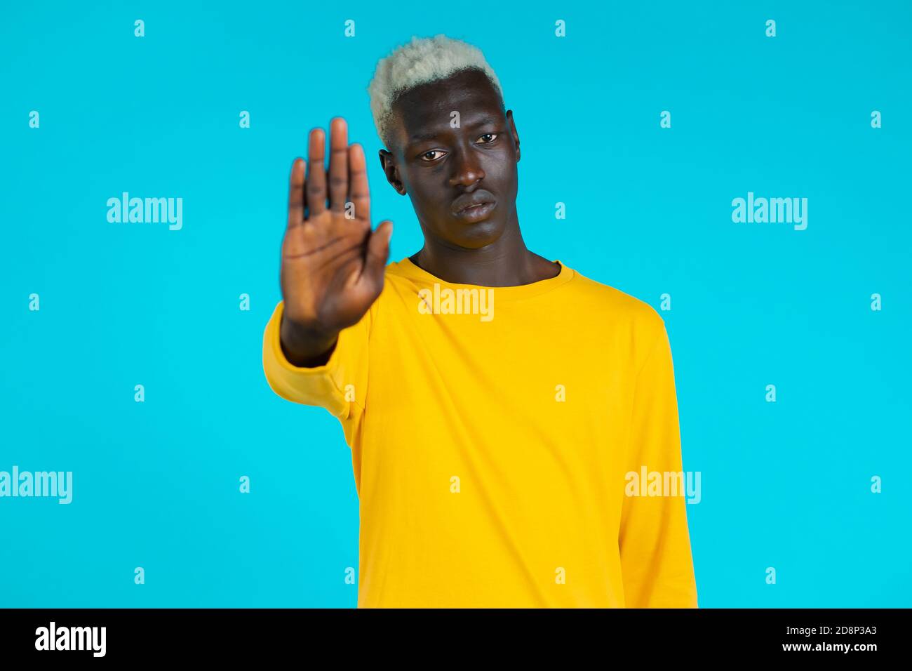 Portrait of serious african american man showing rejecting gesture by stop palm sign. Guy isolated on blue background. Stock Photo
