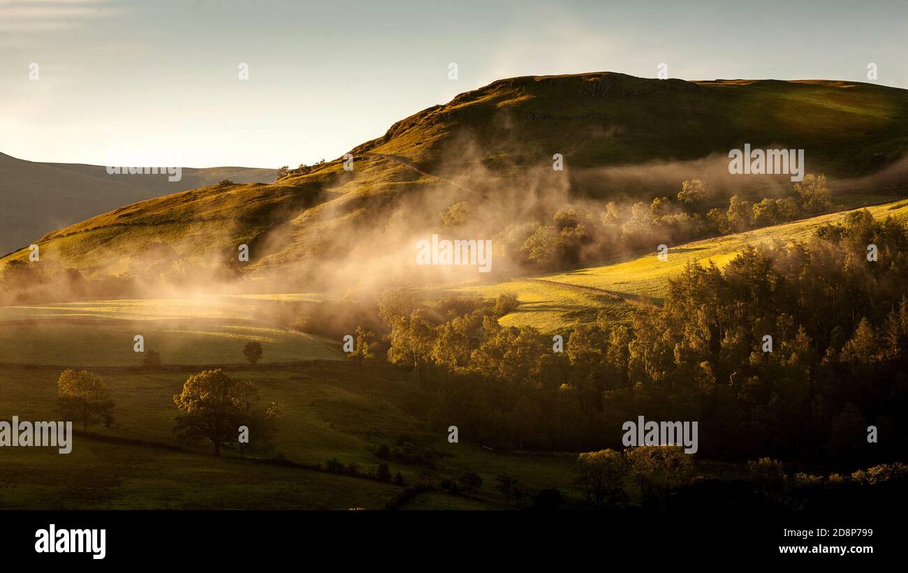 Early morning mist formed on the mountains around Keswick as the sun rises. Stock Photo