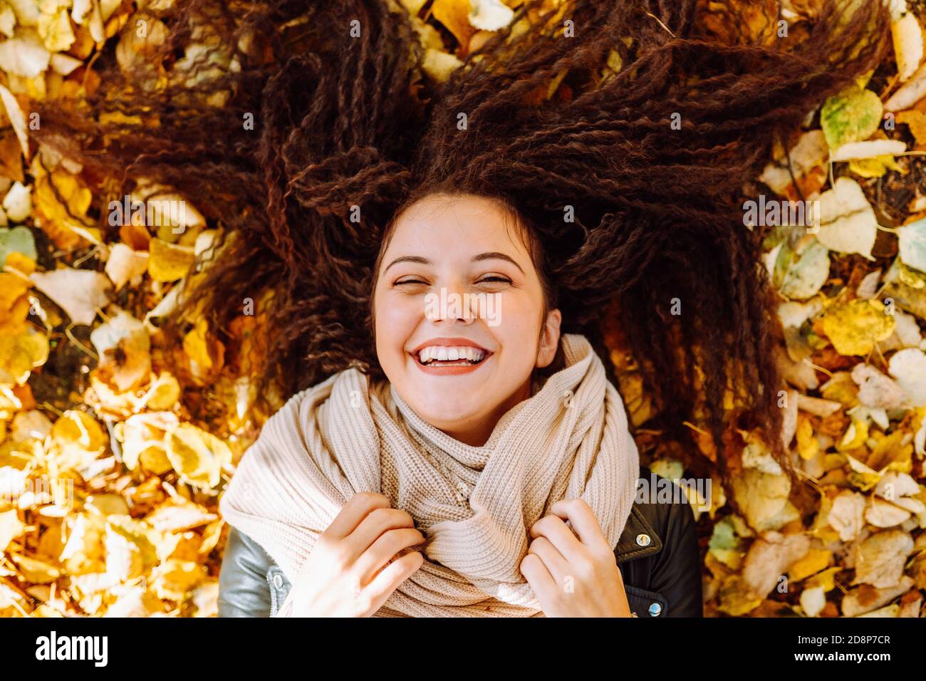 Portrait of beautiful smiling ypung woman lying over yellow leaves at autumn park. Stock Photo