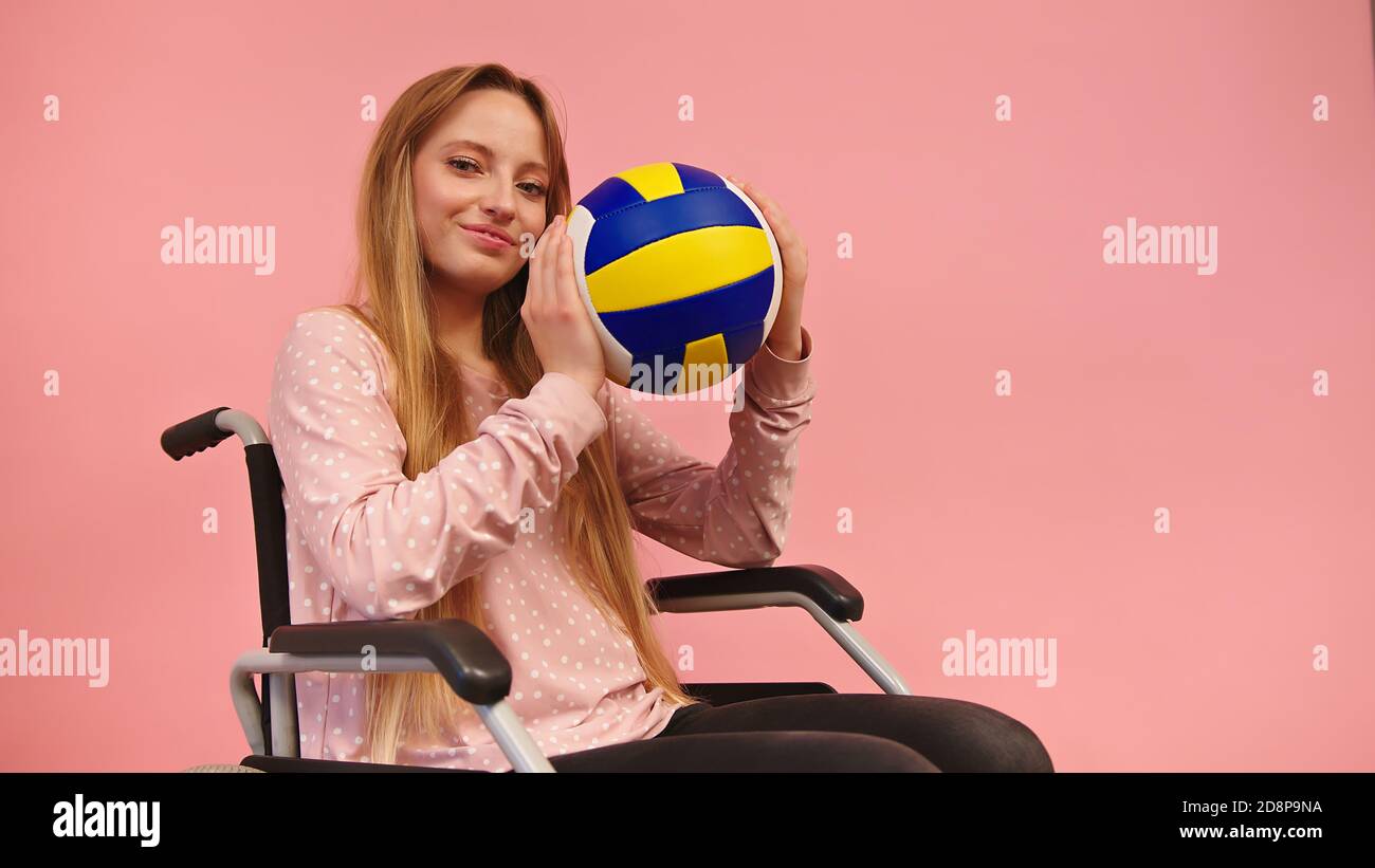 Young Paralympian Woman in Wheelchair Holding Volley Ball and Posing. Positive Handicapped