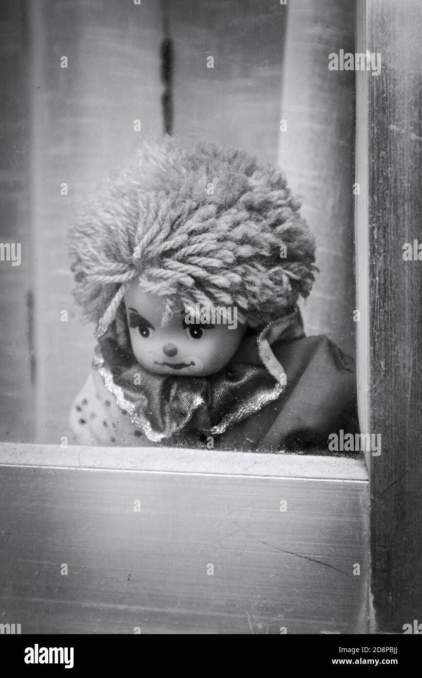 Black and white image of a clown doll who stands looking sadly