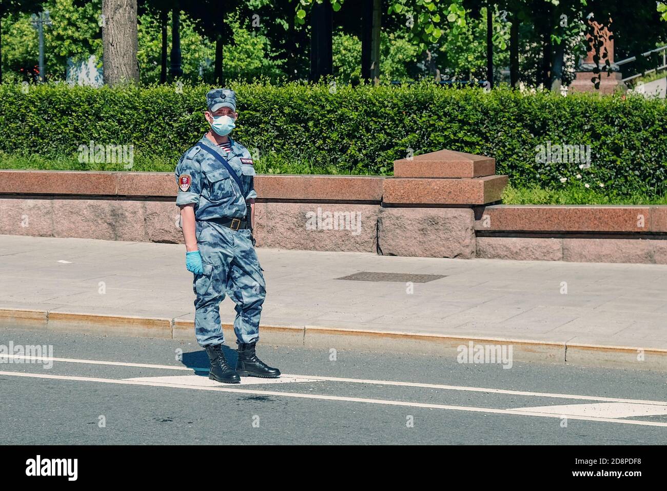 Young soldier of Russia Guard wearing summer camouflage, protective mask and gloves working on the street  Stock Photo