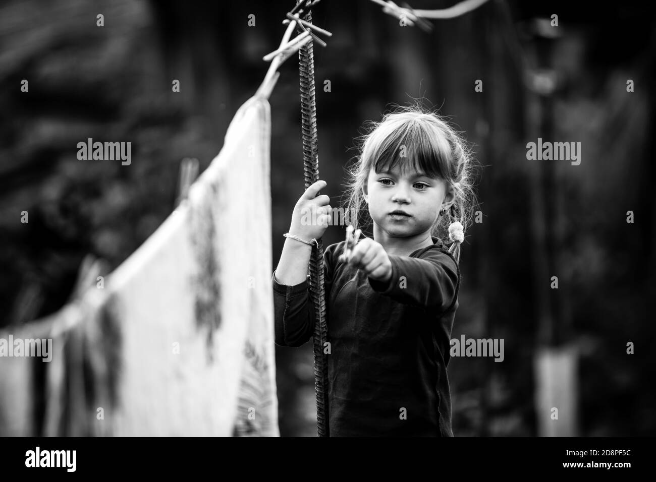 Lovely little five-year girl with clothespin and the clothesline. Black and white photo. Stock Photo