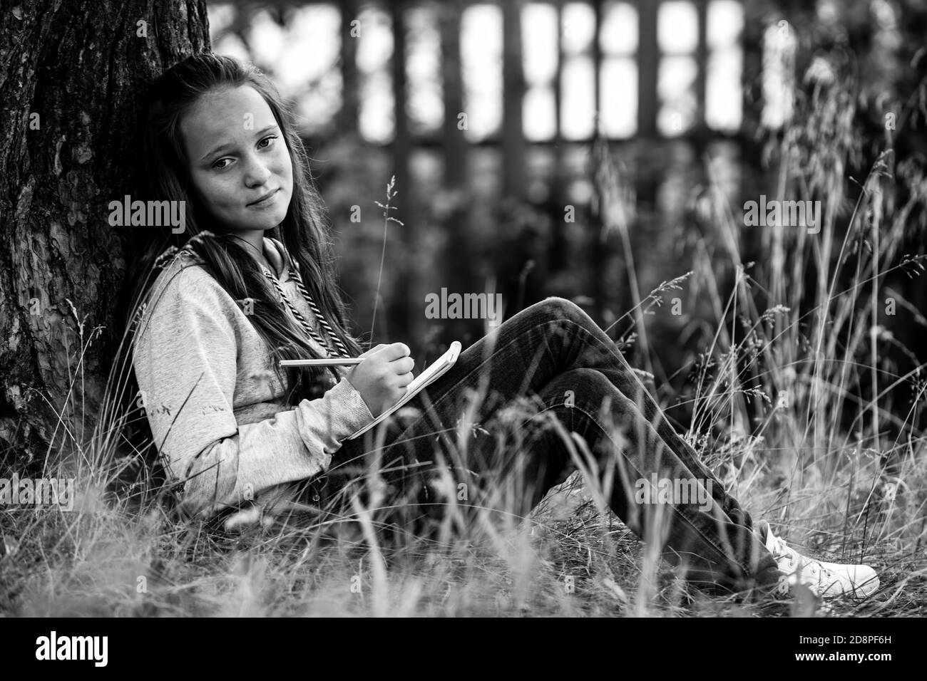 Teen girl writing in a notebook while sitting in the park. Black and ...