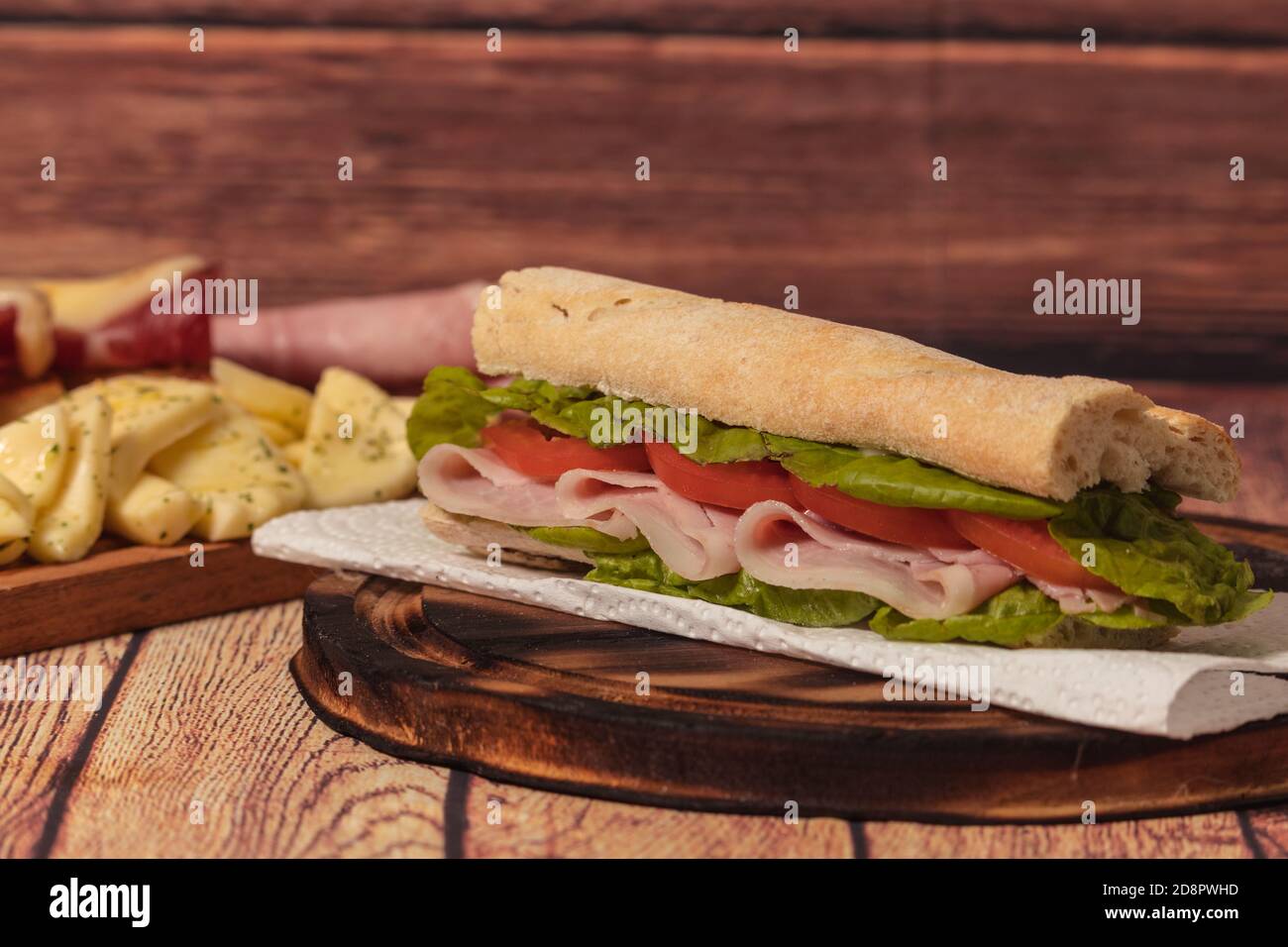 Ham, tomato and lettuce sandwich on a wooden plate on a rustic background Stock Photo