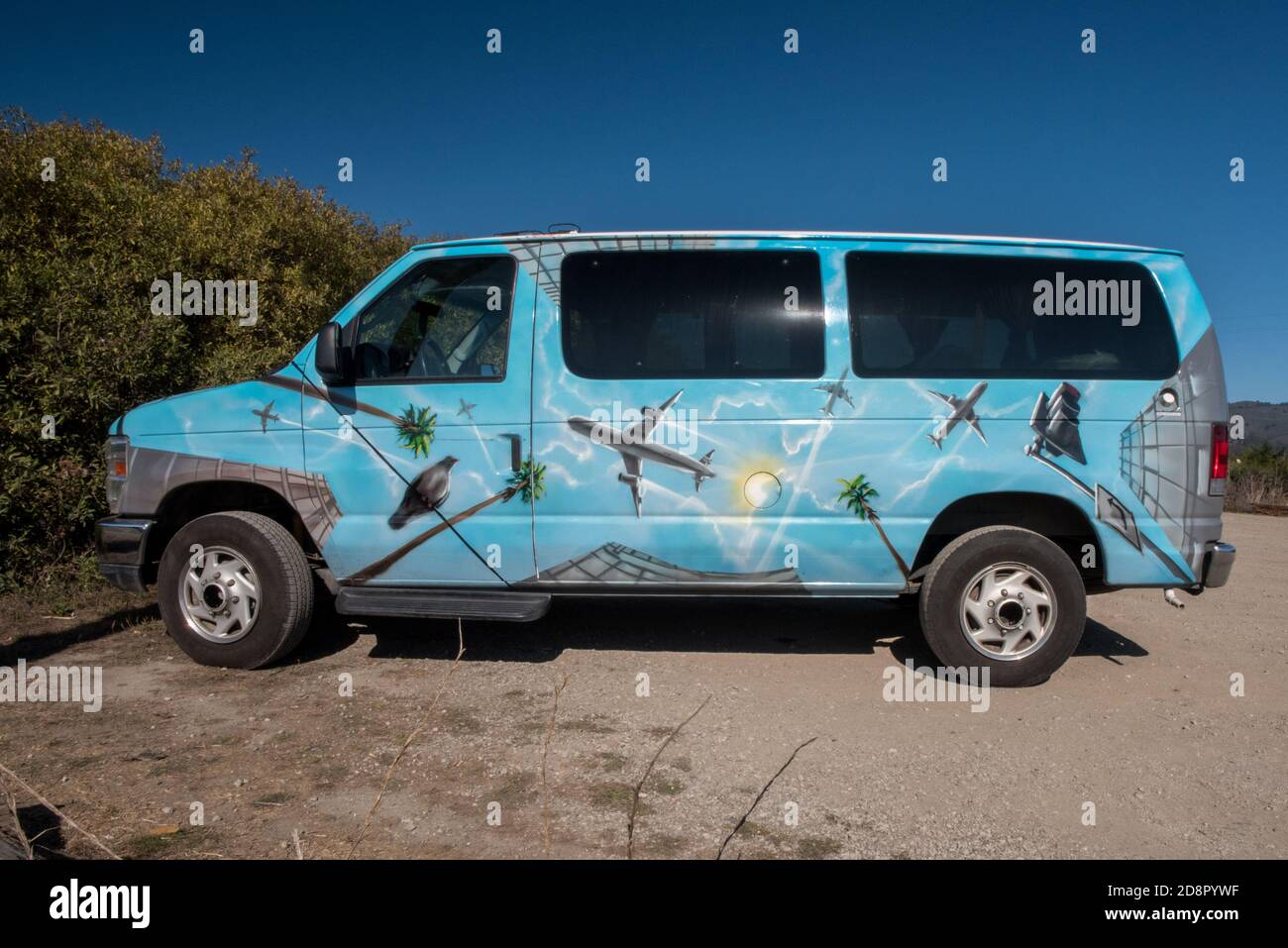 A van painted up with airplanes, palms, and birds parked in a empty lot. Stock Photo