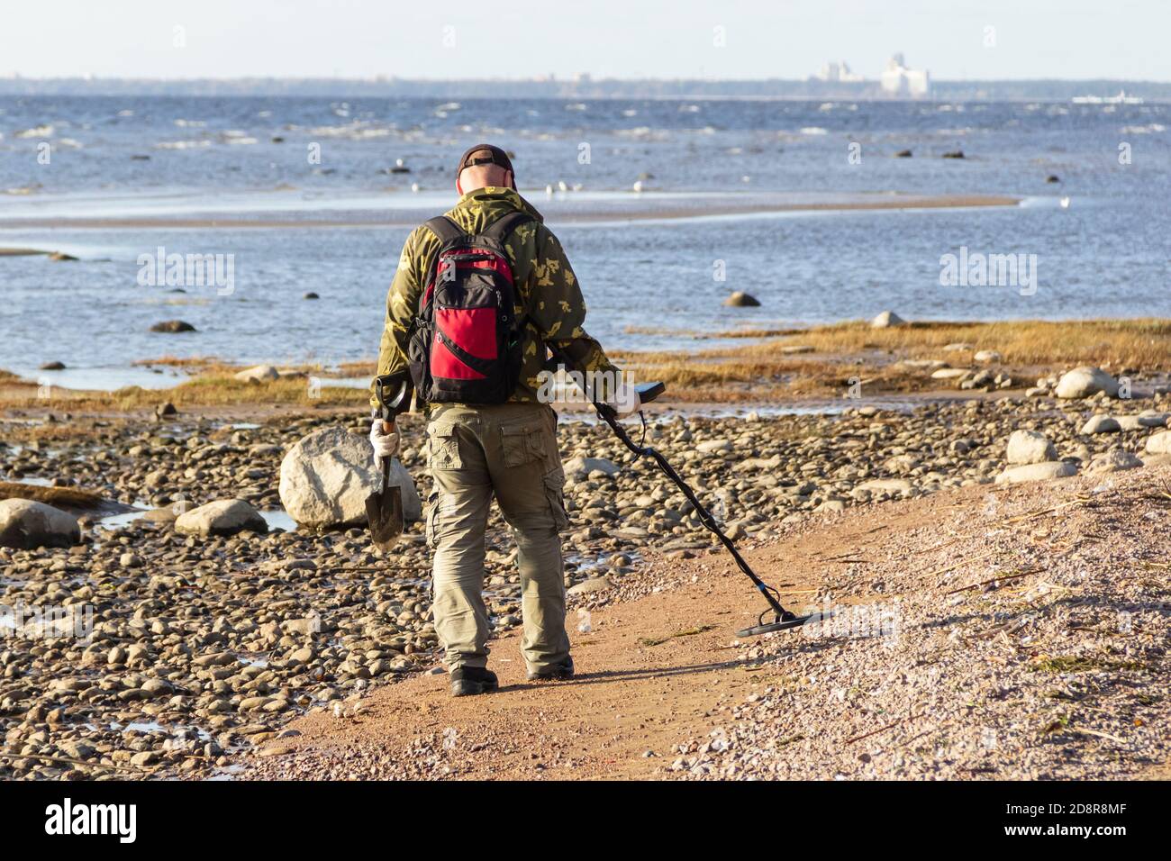 A treasure hunter with a metal detector walks along the sandy deserted beach in search of lost coins and jewelry. Stock Photo