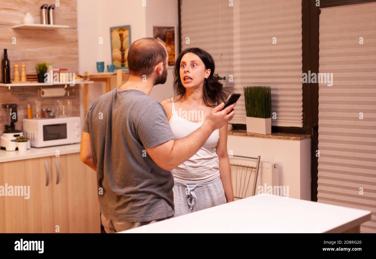 Woman yelling at jelous husband because misunderstanding with texts from phone. Frustrated offended irritated accusing woman of infidelity arguing her with messages. Stock Photo